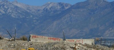 Eine bergige Landschaft, in der ein Überrest einer großen Mauer steht. Auf der Mauer ist ein Graffiti zu sehen. Dort steht: "Private property keep out".
